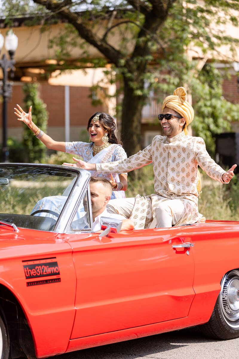 groom rides in back of red convertible for baraat before his chicago ceremony
