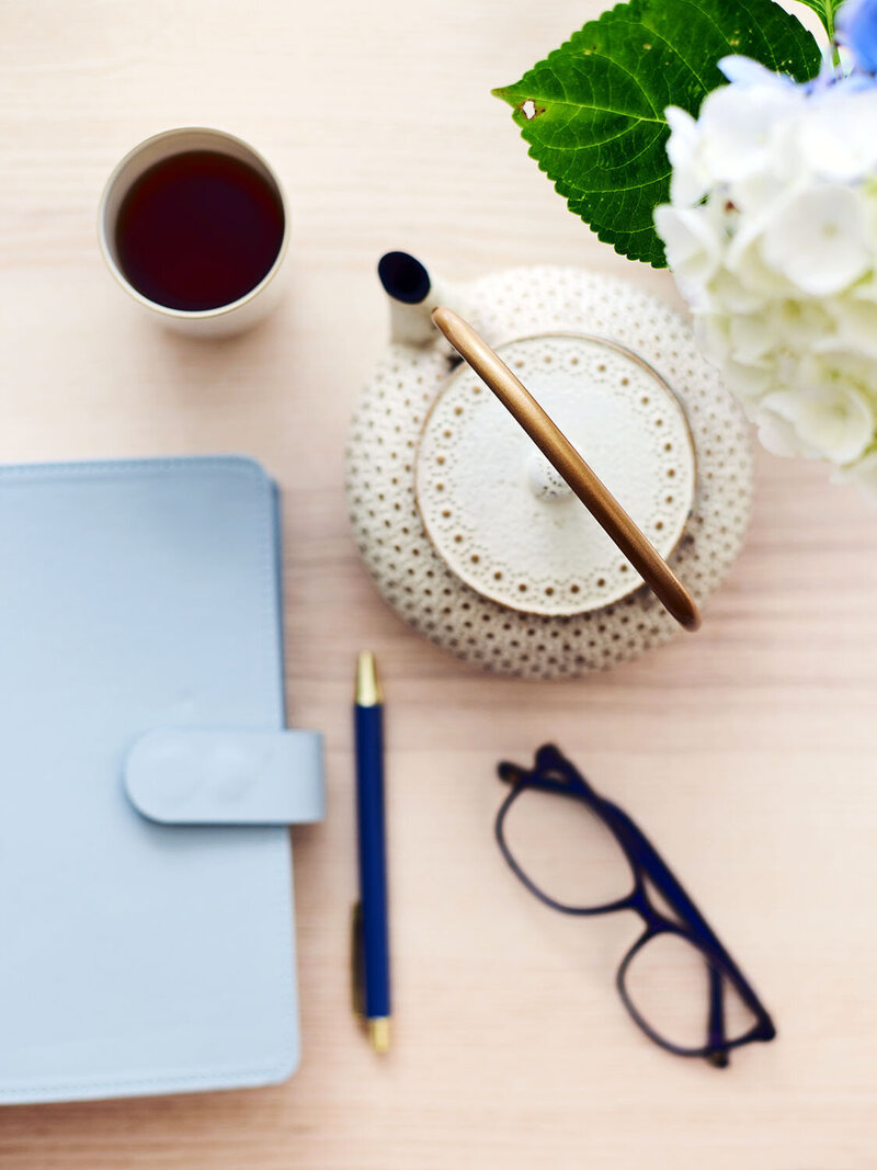 flat-lay of a notebook, pen, glasses and pot of tea