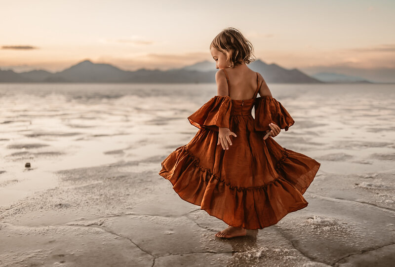 child in a beautiful dress twirling around the slat lake flats in Utah with beautiful mounts as the backdrop