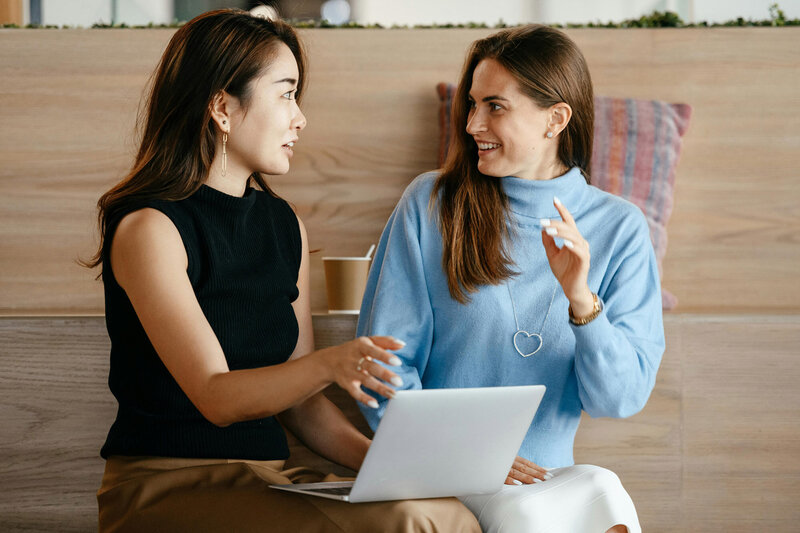 Two women sitting next to each other by a lap top