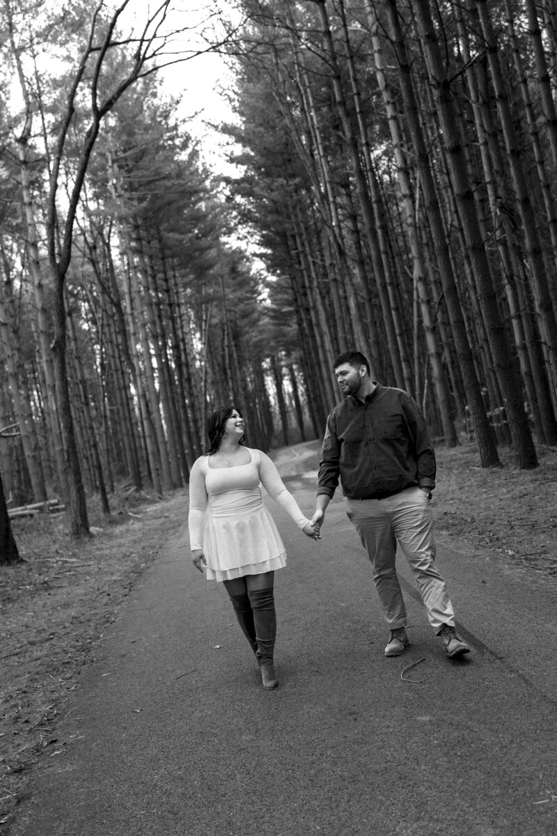 Couple captured in the woods during fall, with bare trees creating a serene, intimate atmosphere, showcasing their love in a quiet setting.