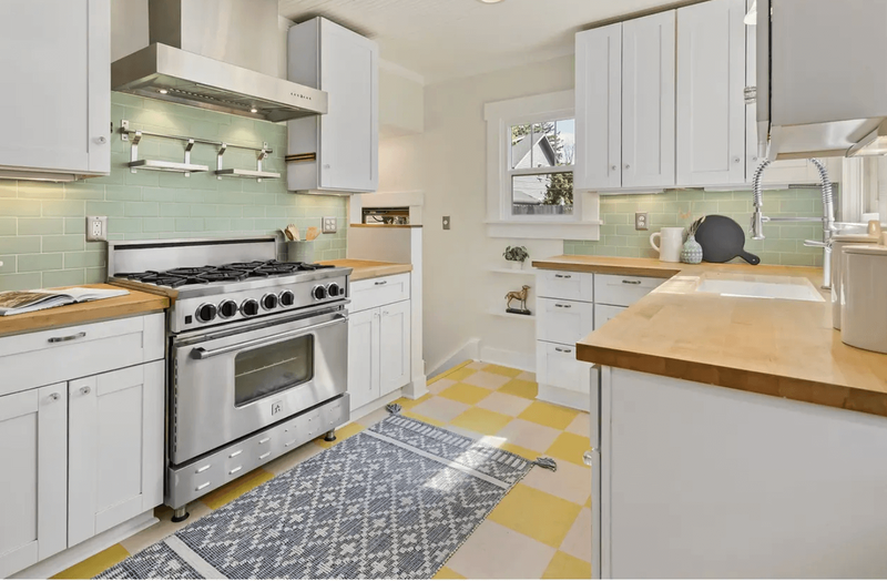 A kitchen featuring white cabinets, yellow and cream tiled floor and a large oven.