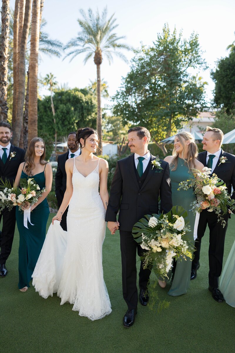 bride and groom walk hand in hand alongside wedding party