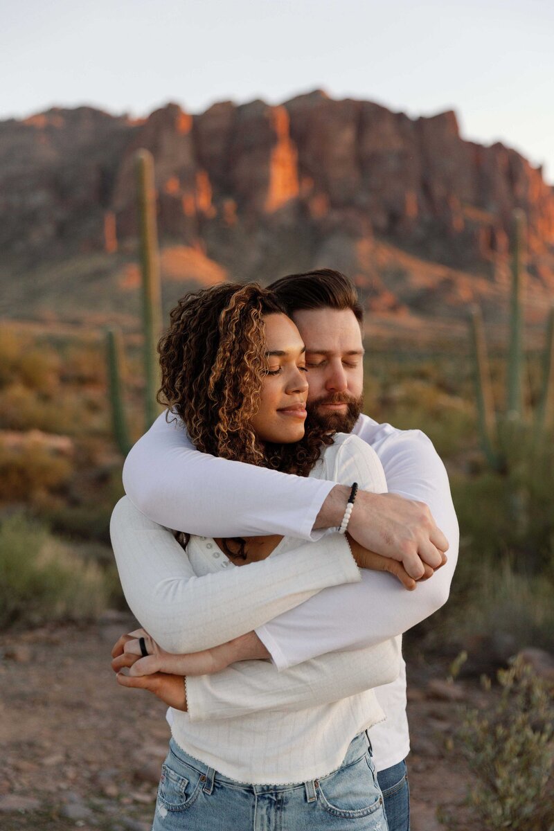 Couple cuddles together while watching the desert sunset.