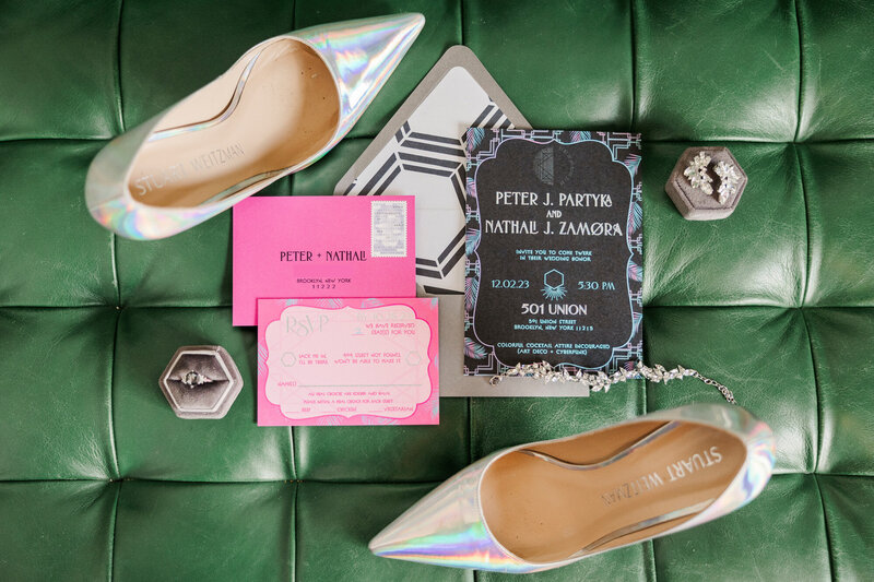 A black and holographic wedding invitation suite with hot pink wedding rsvp card next to holographic wedding heels.