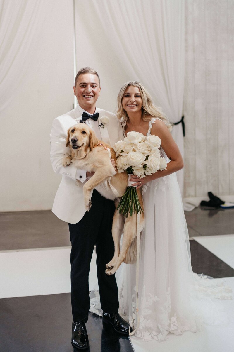 Bride and groom hold dog ring bearer after the ceremony at their black tie celebration