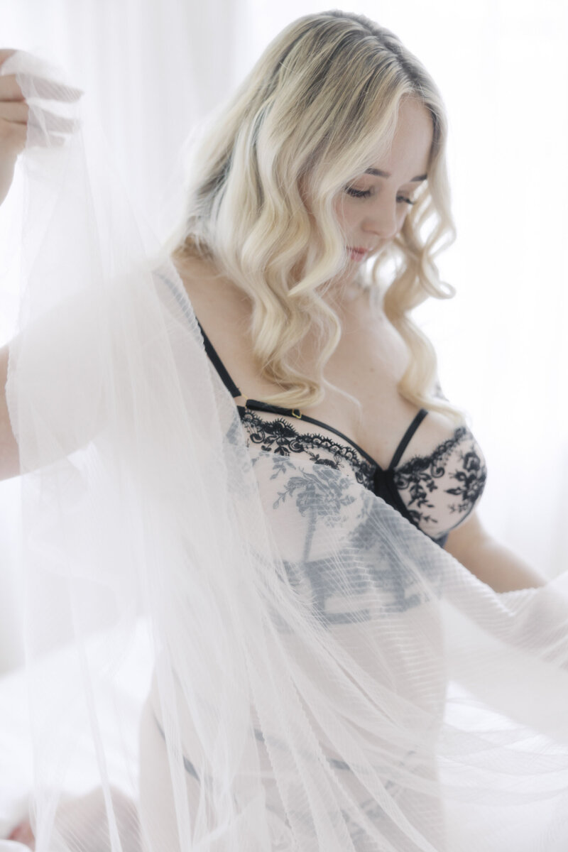 Black and white bridal boudoir portrait of a woman wearing a black lace gown