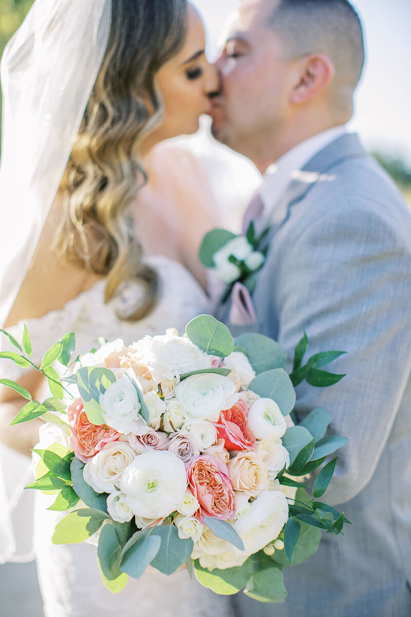 13-radiant-love-events-closeup-bride-groom-kissing-blurred-in-background-bouque-white-pink-flowers-in-focus-romantic-elegant-timeless