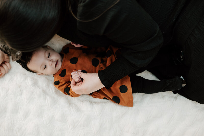 Milestone photo of 6 month baby girl laying with mom on blanket wearing orange and black in Annapolis Maryland.