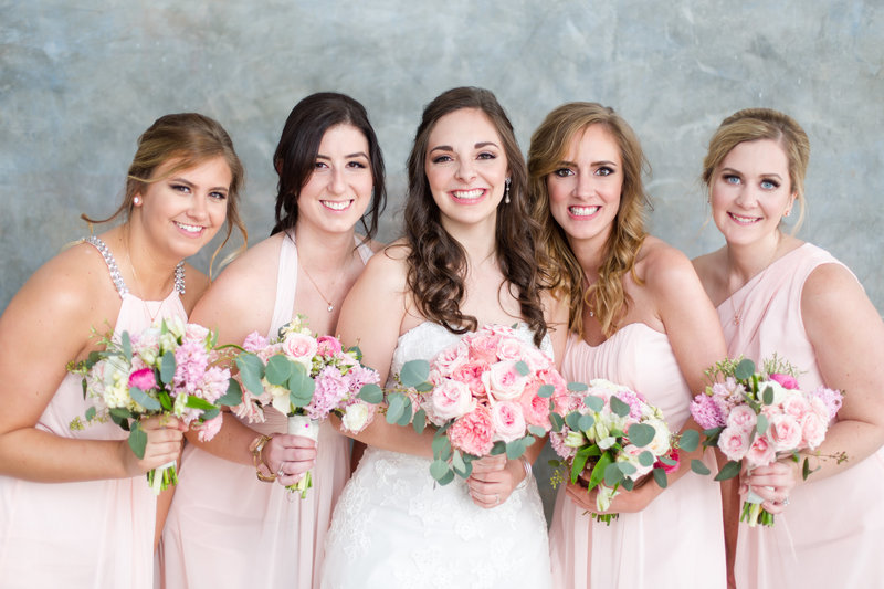 Bridesmaids in light pink dresses with bride all holding pink peony bouquets