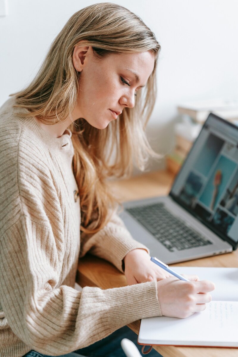 Gros plan sur une jeune femme à son bureau qui écrit à la main sur un carnet