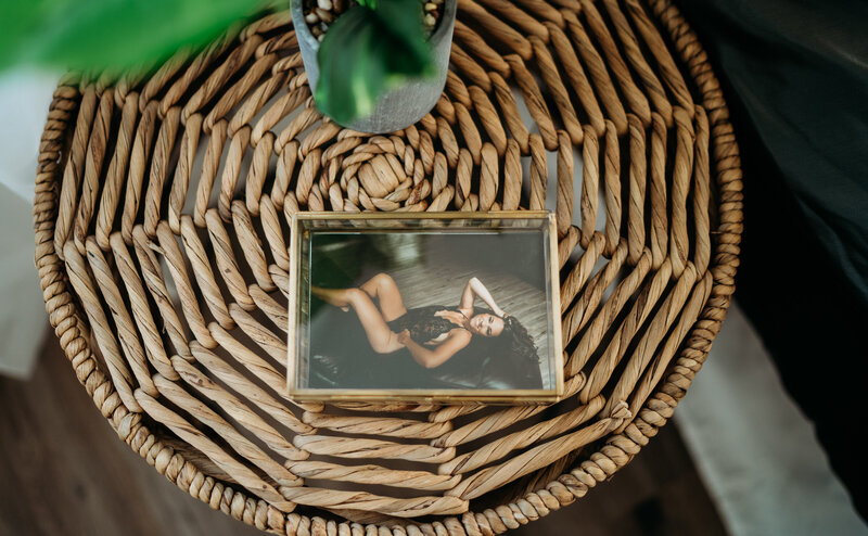 Small prints of a woman in black lingerie sit in a glass box on a wicker bedside table