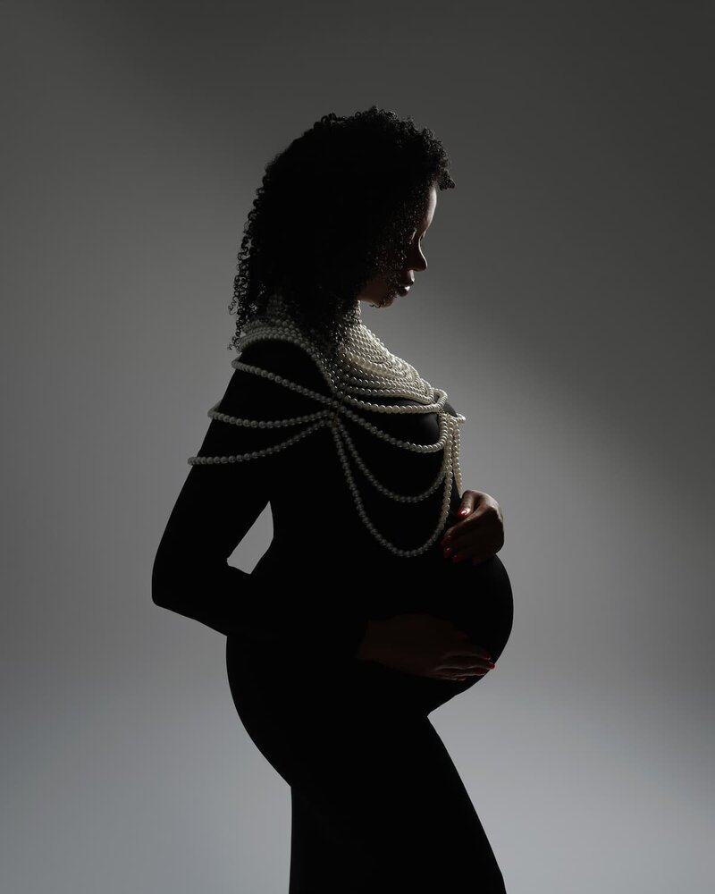 Studio maternity photo of a pregnant woman wearing layered pearl necklaces – available at Hello Photography Austin