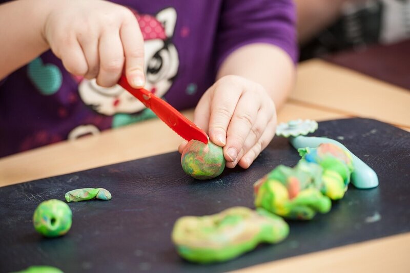 small child cutting colorful clay pieces