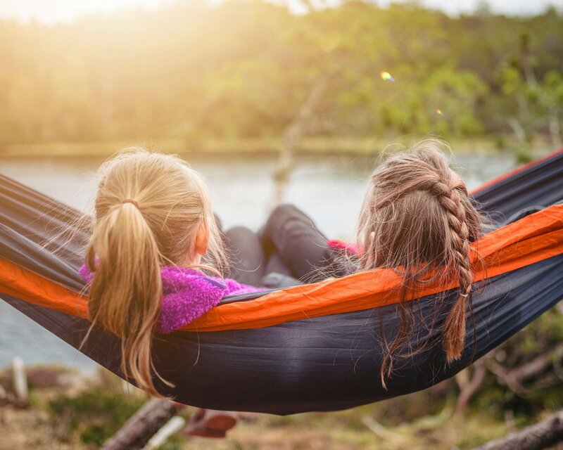 Two friends swinging in a hammock enjoying time outside by the water