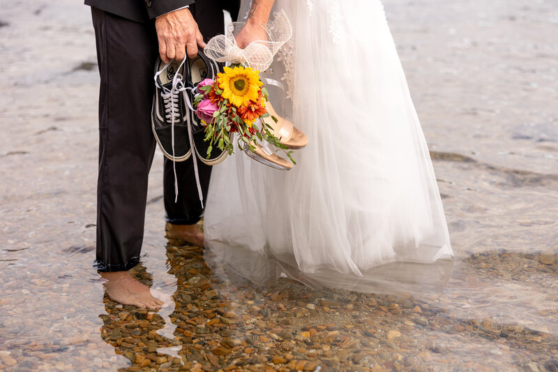 Bride and Groom close up of feet in the water holding shoes and bouquet