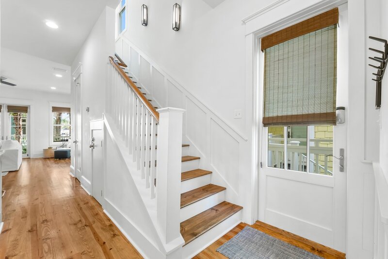 Entry hallway with wooden stairs and bright white interiors at Tangerine Dream vacation rental in Panama City Beach.