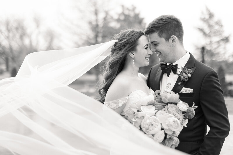 A black and white photo of a bride and groom with the veil flowing in the wind