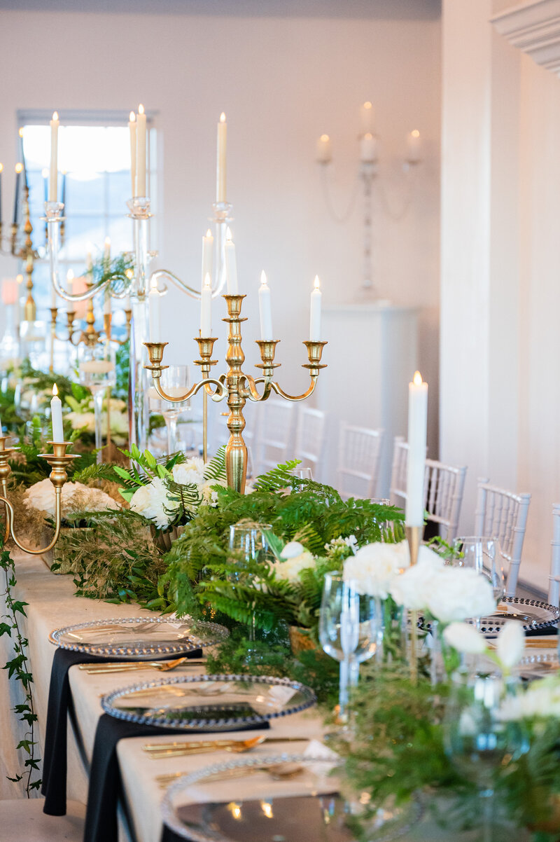 A white table scape at a tented reception with white florals and clear chairs.