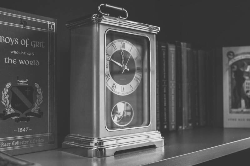 black and white of a golden table pendulum clock and books on a bookshelf