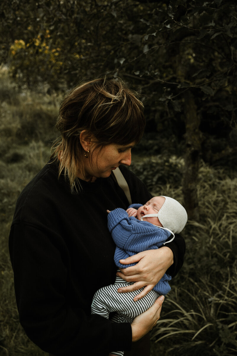 Portret van fotograaf lieselot in haar tuin die haar pasgeboren dochter paula vast heeft.