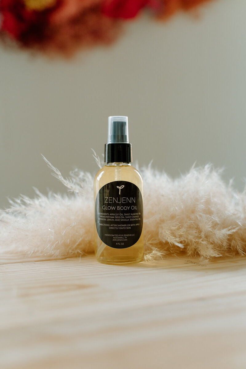Product photo of body oil on wood table, styled with pampas grass and soft lighting.