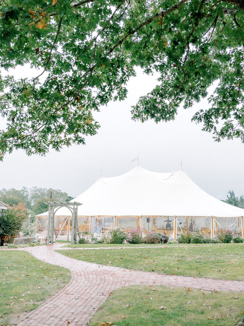 Large white reception tent with greenery and florals in the grass around it