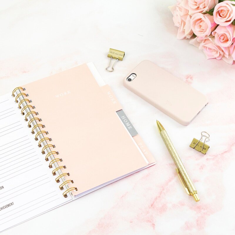 blush pink notebook, pink phone, gold pen, and gold paper clip on pink water color mater