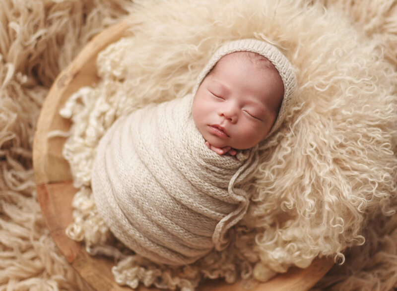 newborn boy swaddled in a hand knit wrap and nestled in a vintage wooden bowl with a variety of furs and textures  newborn boy swaddled in a hand knit wrap and nestled in a vintage wooden bown with a variety of furs and textures