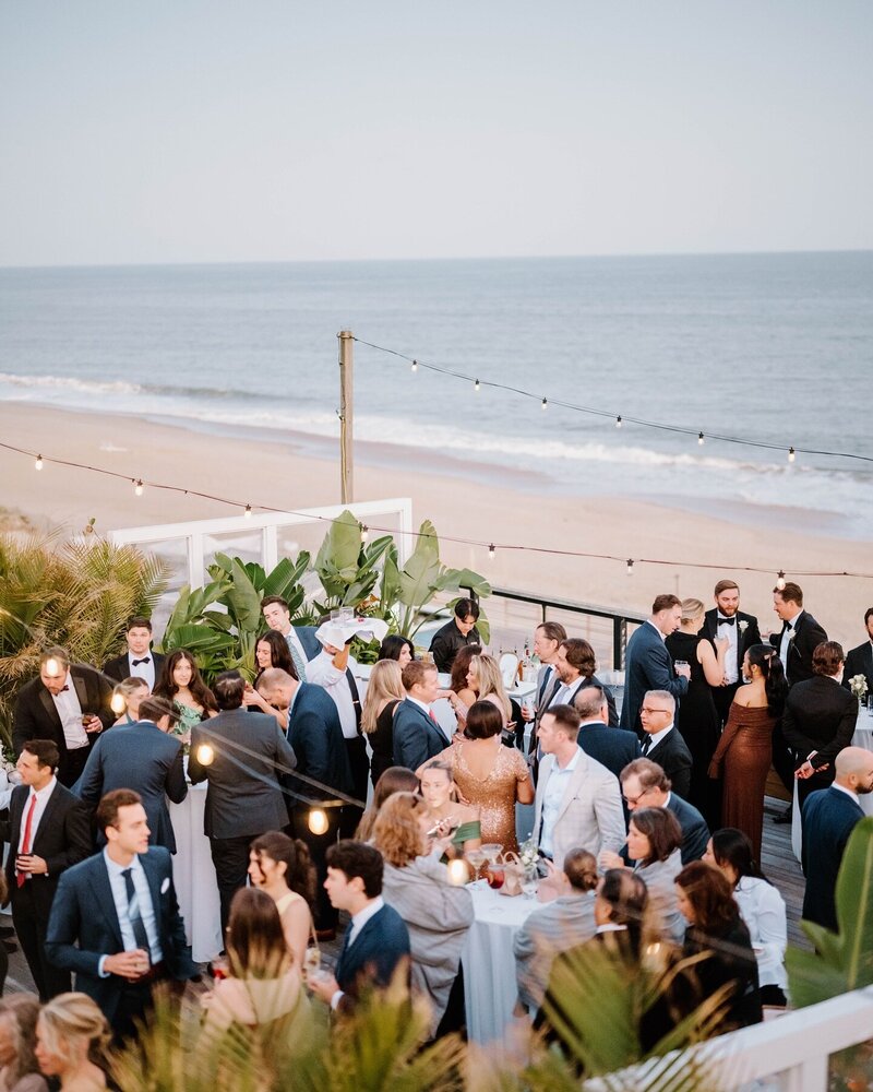 Rhode Island Wedding Photographer | A beachside evening event with elegantly dressed guests mingling near string lights. 