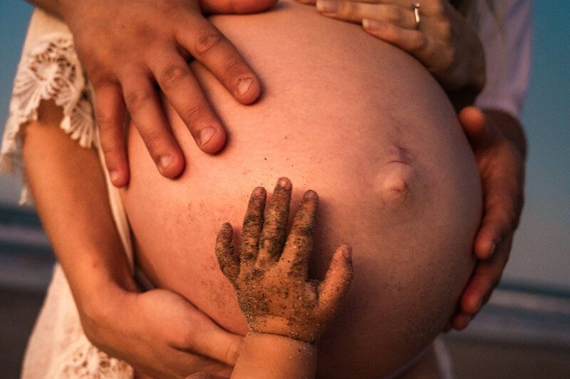 big pregnant belly with hands on it at the beach with sand