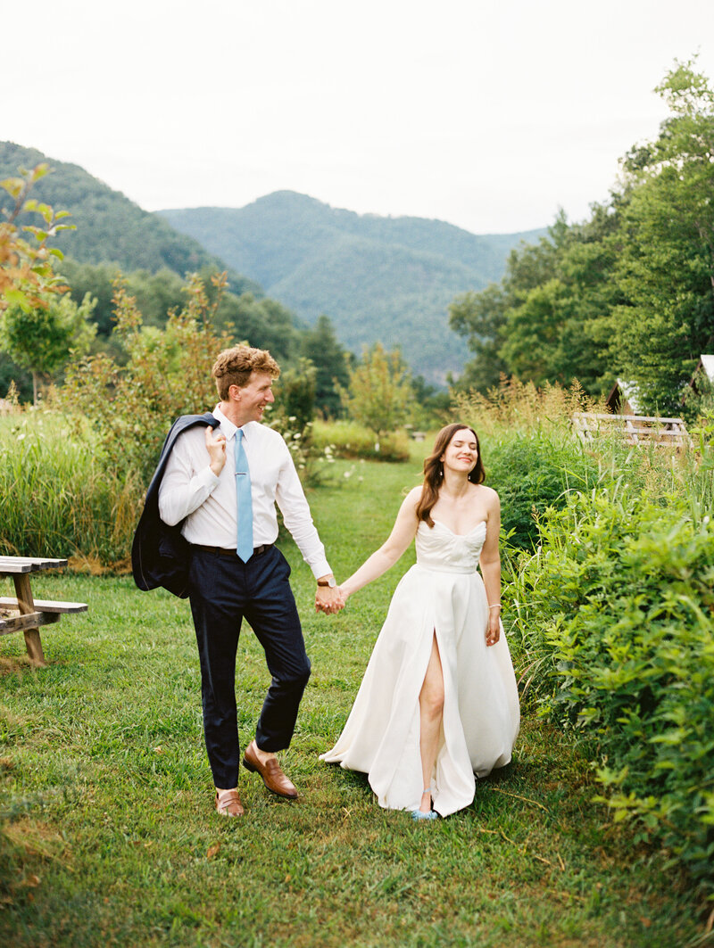 Holding hands, the bride and groom walk among the lush nature of Paint Rock Farm, a scenic wedding venue in North Carolina, by destination photographer Megan Lynn of My Sun and Stars Co.