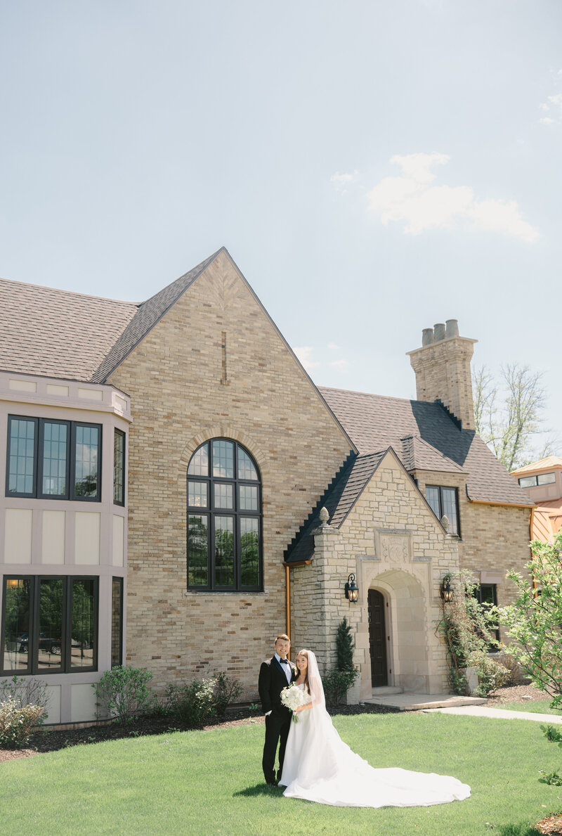 A couple stands in front of a stone manor on their wedding day in the spring time.