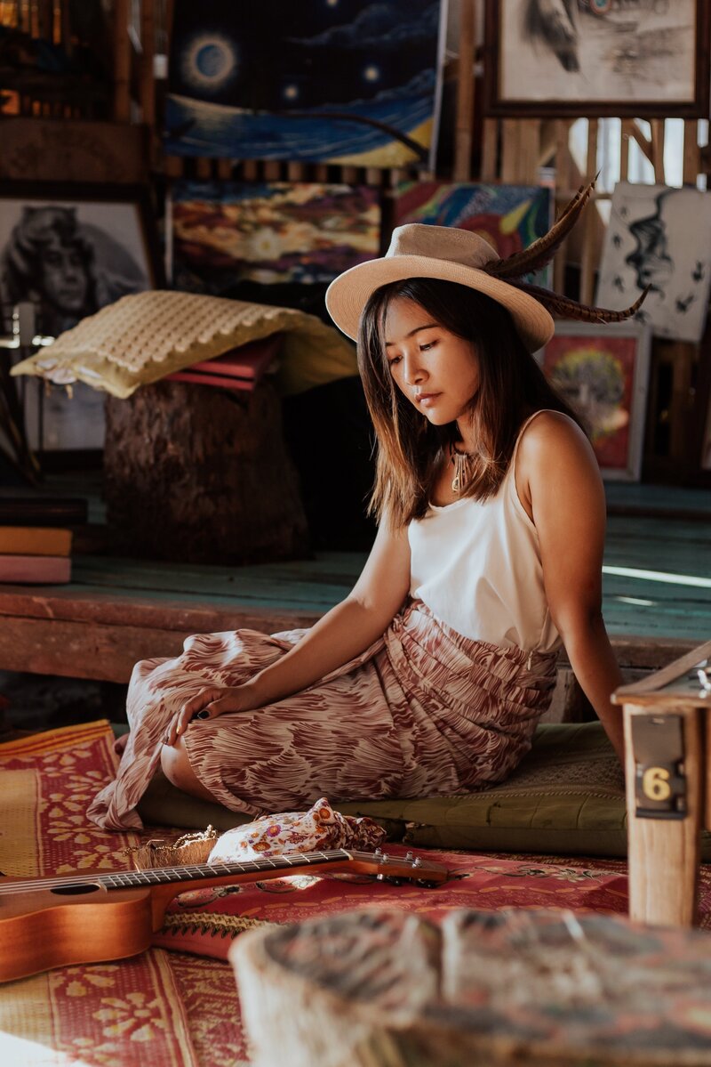 A woman in a tank top and flowing skirt sits on the floor looking down at an Oracle Card spread