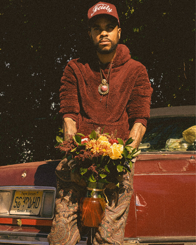 man in faashionable streetwear holding a vase with a beautiful bouquet of flowers and the main logo for dirty stems