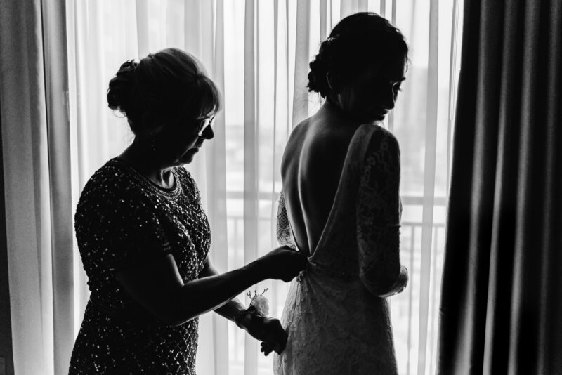 Bride puts on her wedding dress in front of window