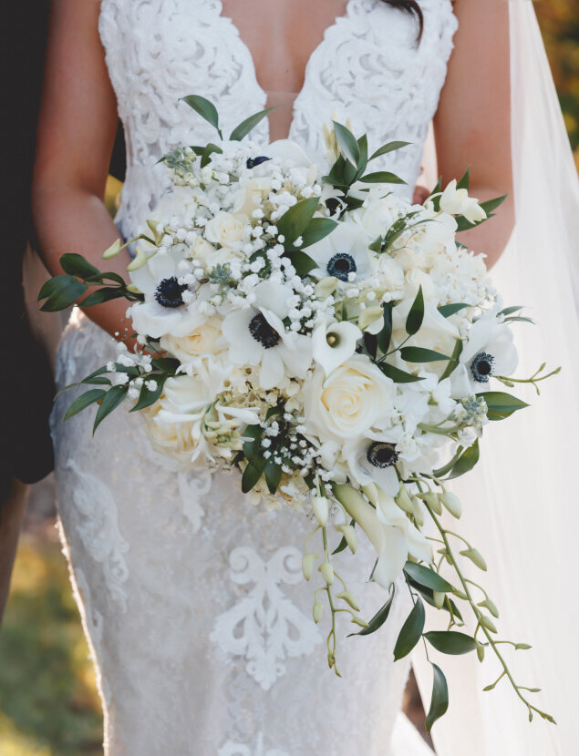 A close up from the chest down to the knees of a bride holding a wedding bouquet of white flowers.