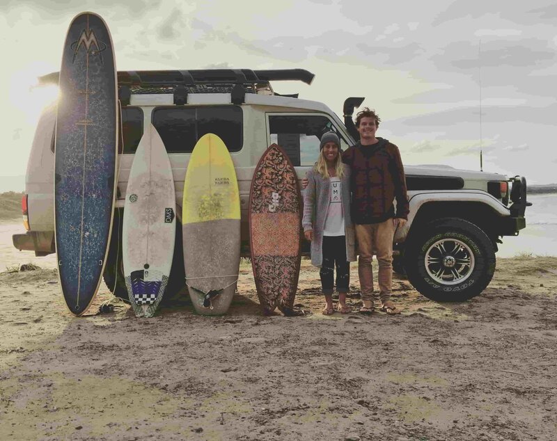 Surf boards against troopy on beach smiling owners