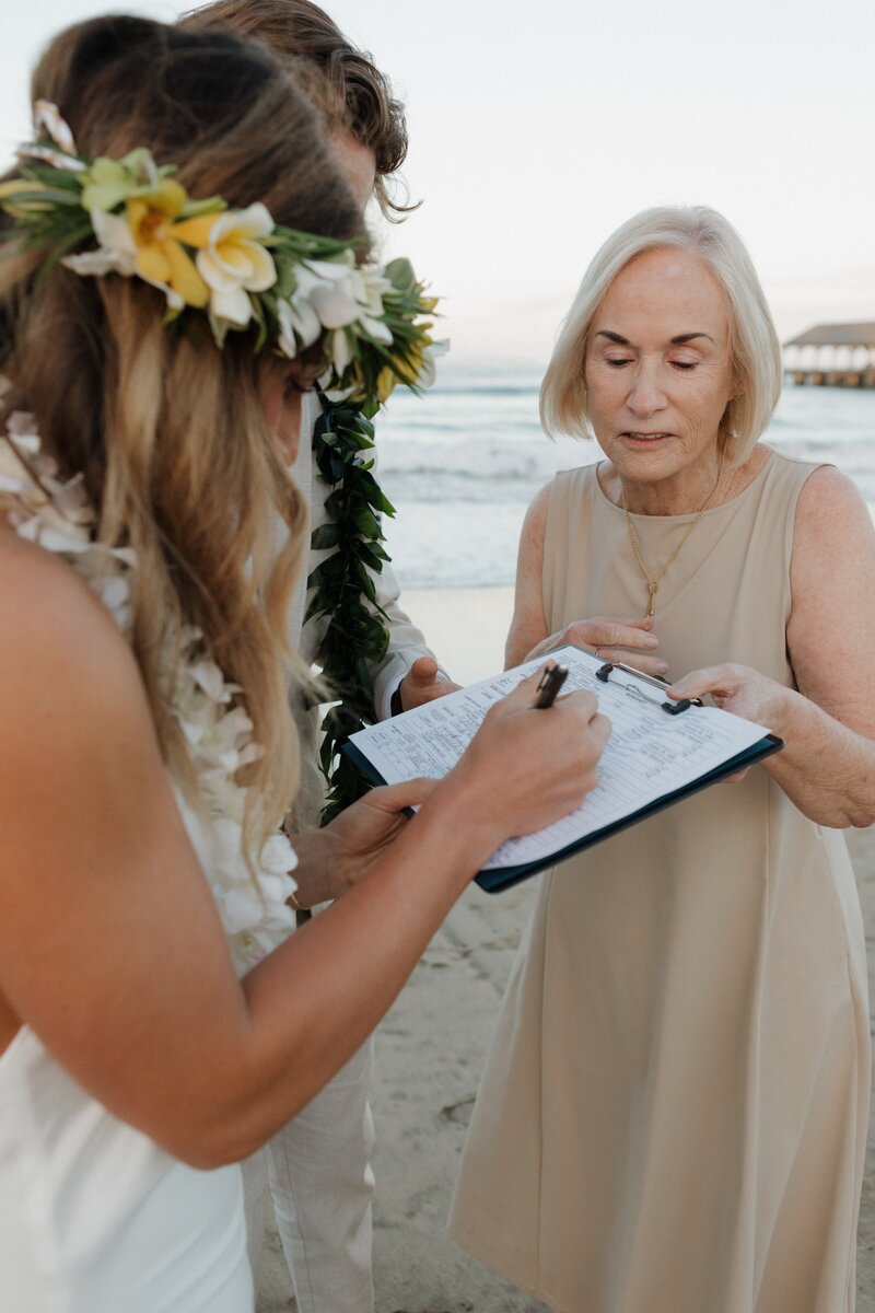 bride on beach in hawaii signing marriage certificate