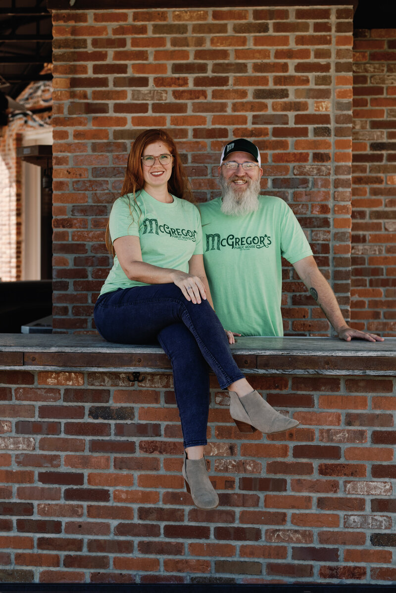 Irish pub owners Meagan and Tom McgGregor sitting in frotn of brick wall at the outside bar of their pub location.