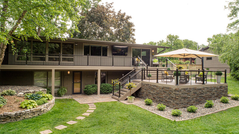 Wide view of a square deck with two short staircases, one leading to the ground and the other leading to a catwalk that spans the length of the house. 