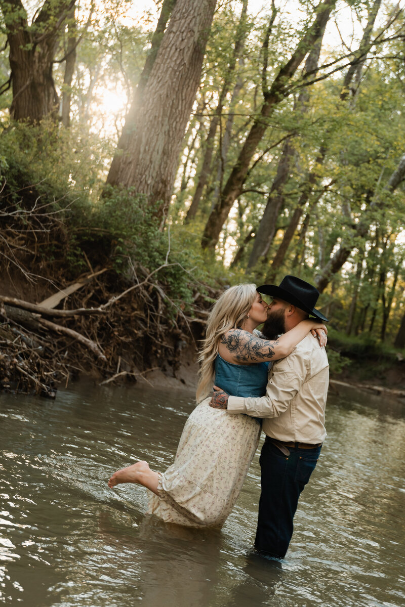 Couple sharing a tender moment near a creek, surrounded by nature, captured in a beautiful outdoor setting.