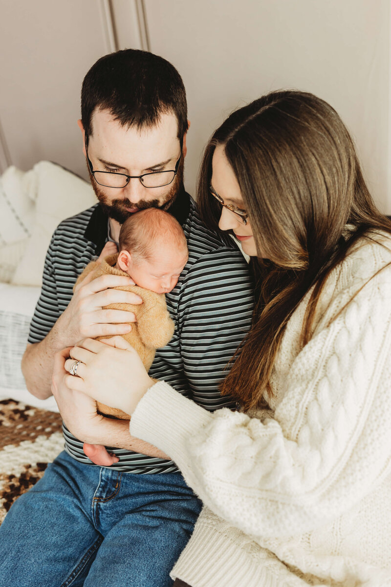 mom in a floral dress and dad in a green henley holding their newborn boy with their eyes closed