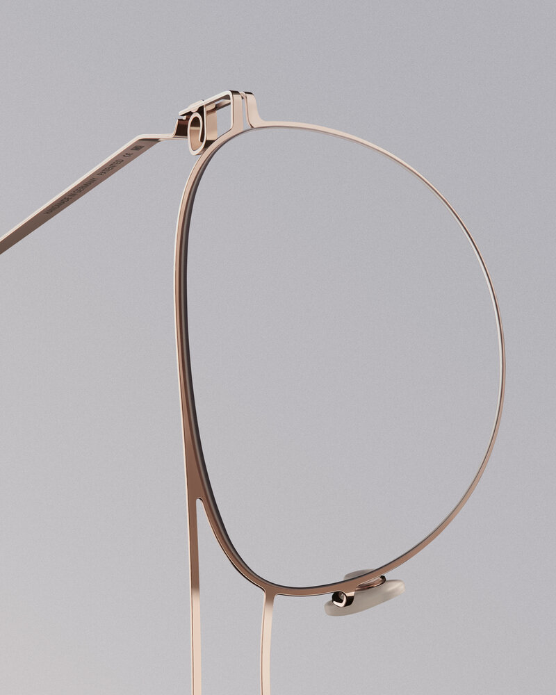 Very close-up shot of one lens of a pair of thin-framed rose gold glasses on a gray background