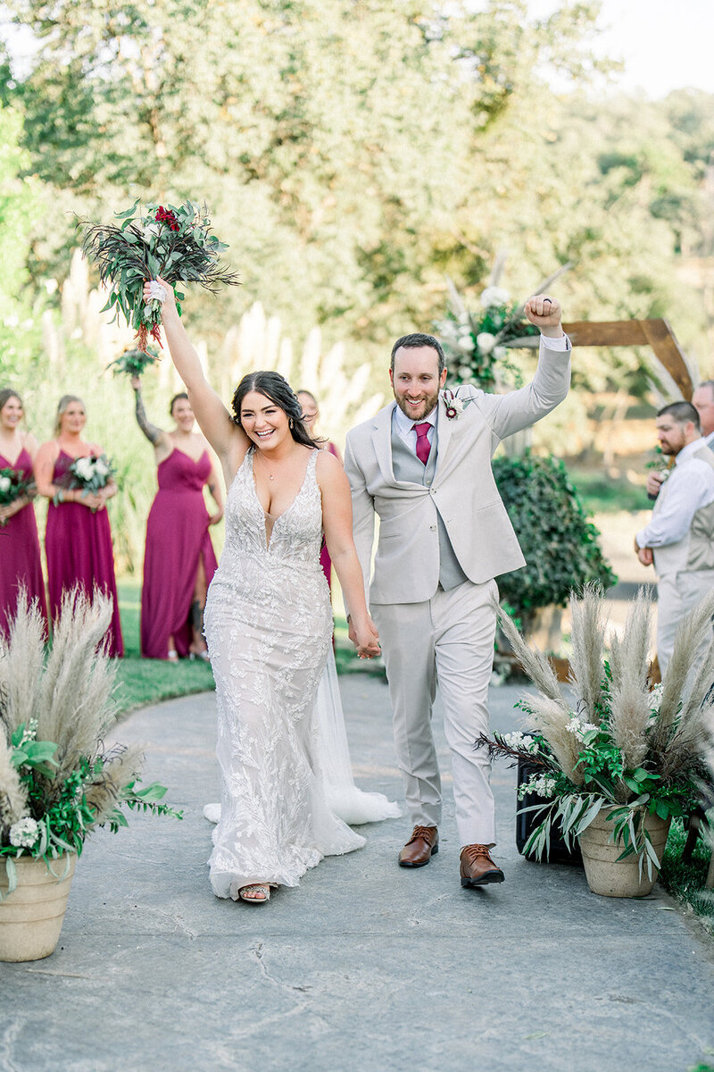 Tiffany Longeway Photography captures the exuberant joy of a newlywed couple at Charles Krug Winery in Napa Valley. With the bride raising her bouquet triumphantly and the groom beaming with happiness, this image reflects the vibrant and festive spirit of a wedding at one of Napa Valley’s oldest and most renowned wineries. Perfect for couples seeking a picturesque and celebratory venue for their special day.