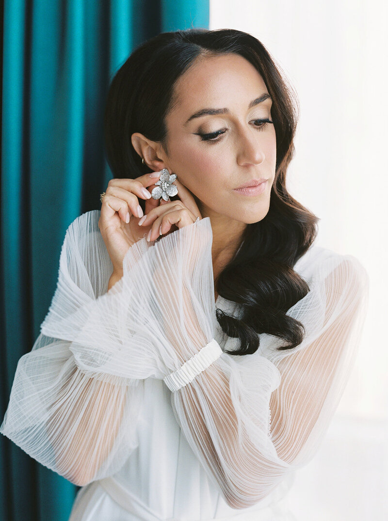 Bride putting on her earrings while getting ready for her editorial wedding photography.