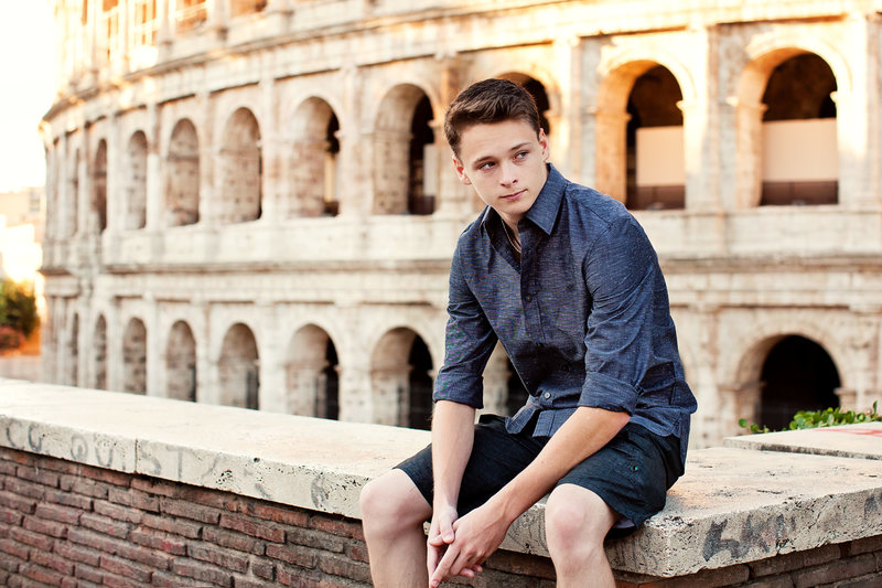 A guy sitting on a ledge in front of the Colosseum. Taken by Rome Solo Travel Photographer, Tricia Anne Photography