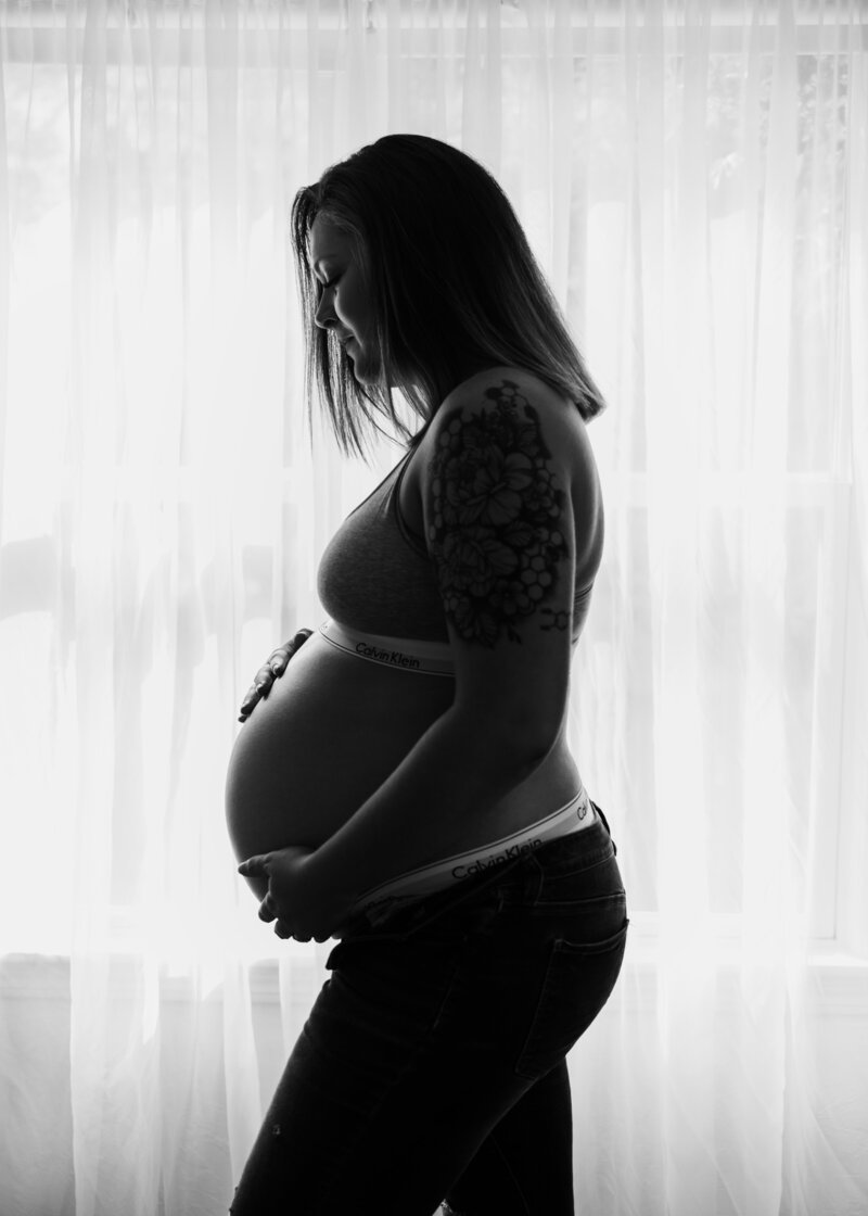 Jordan Hill stands by the window while admiring her pregnancy belly.