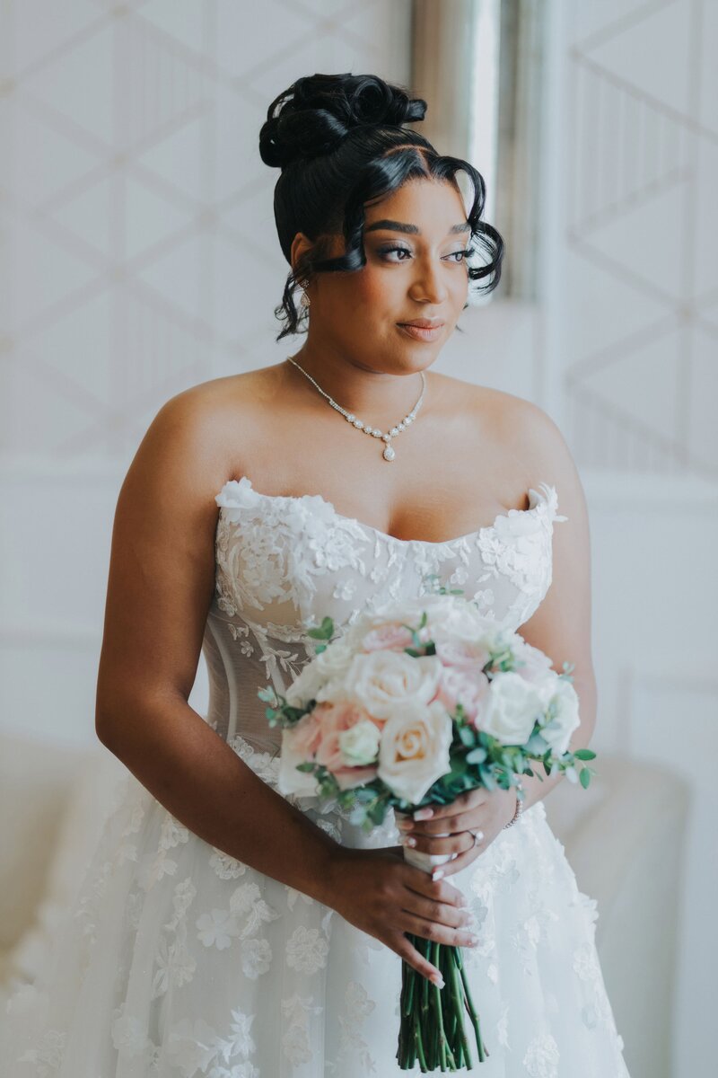 Bride gazes out a window in white wedding dress.