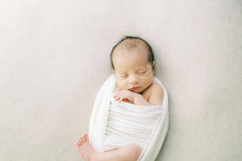 Newborn baby swaddled in a white swaddle and sleeping